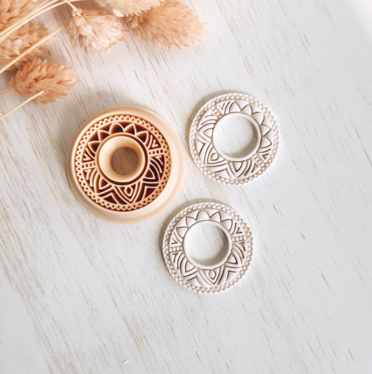 Decorative circular objects with intricate patterns on a light wooden surface with dried plants.