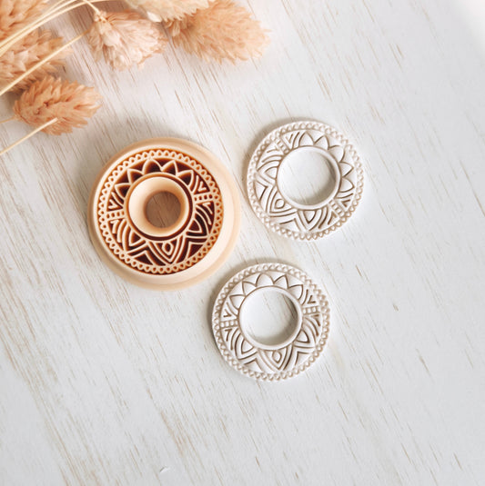 Decorative circular objects with intricate patterns on a light wooden surface with dried plants.